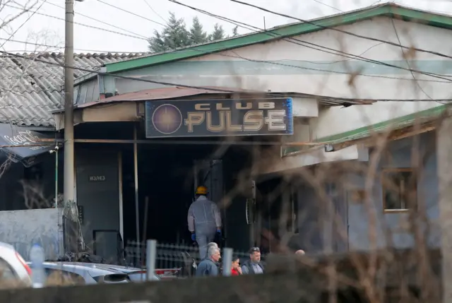Profissional equipado com roupa de segurança entra em local com vestígios de fogo, com o letreiro Club Pulse